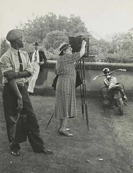 Photographer Frances Benjamin Johnston standing beside her view camera preparing to take... 1938. Creator: Unknown