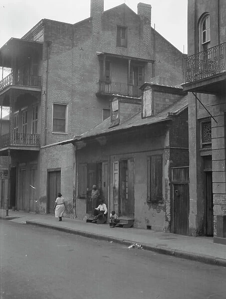 View from across street of a man and child sitting on steps and a woman walking down... c1920-1926. Creator: Arnold Genthe