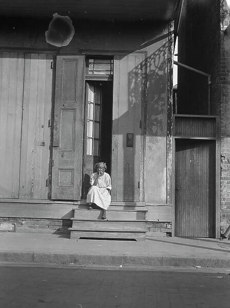 View from across street of a woman sitting on steps, New Orleans, between 1920 and 1926. Creator: Arnold Genthe