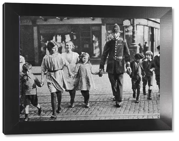 Policeman helping schoolchildren across the road, East End, London, 1926-1927