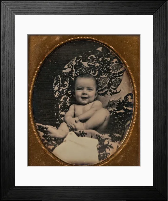 Framed Print : [Smiling, Nude Baby Holding Foot, Seated on Furniture Draped with Floral Print Fabric]