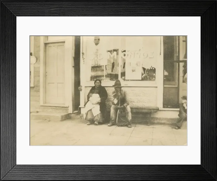 Framed Print : Photograph of a man and woman sitting outside of a storefront, early 20th century Framed Print : Photograph of a man and woman sitting outside of a storefront, early 20th century