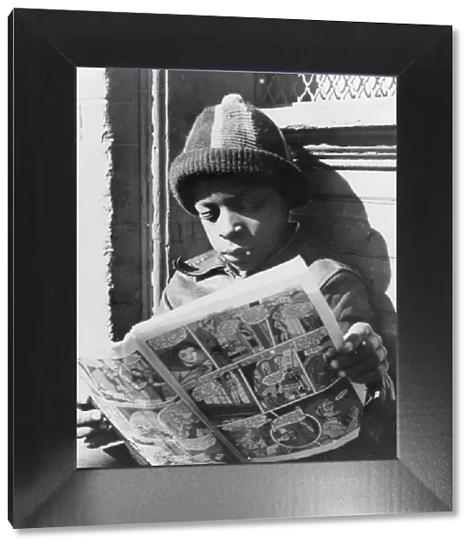 Negro youth reading a funny paper on a door step in the Southwest section, Washington, D. C. 1942. Creator: Gordon Parks