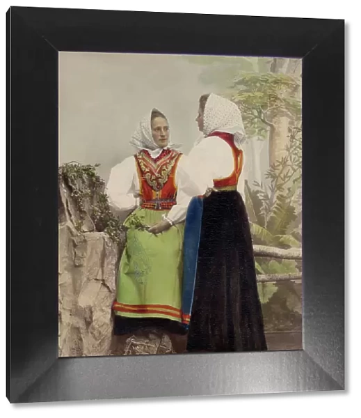 Two young women pose in folk costumes, with dotted headdresses, 1886-1890. Creator: Helene Edlund
