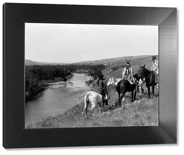 Three Piegan Indians and four horses on hill above river, c1910. Creator: Edward Sheriff Curtis