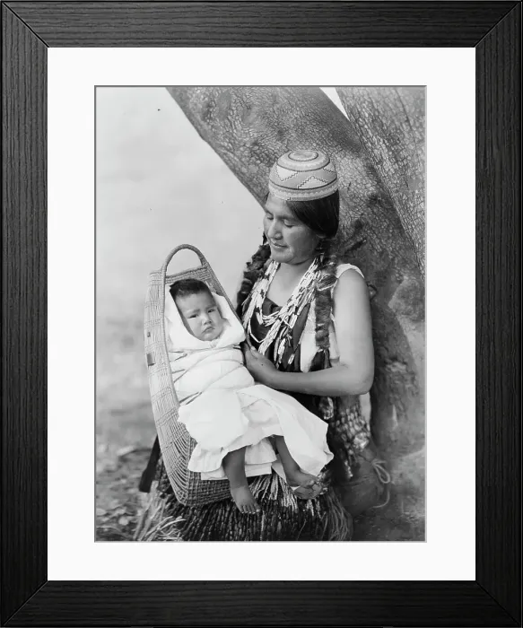 Framed Print : Hupa mother, three-quarter length portrait, seated, facing left, holding baby, c1923. Creator: Edward Sheriff Curtis