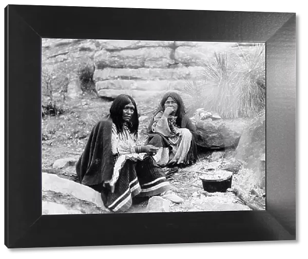 Two Apache Indian women at campfire, cooking pot in front of one, c1903. Creator: Edward Sheriff Curtis