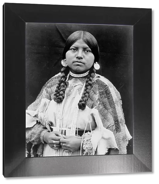Cayuse woman, half-length portrait, standing, facing front, braids, shell disk earrings... c1910. Creator: Edward Sheriff Curtis