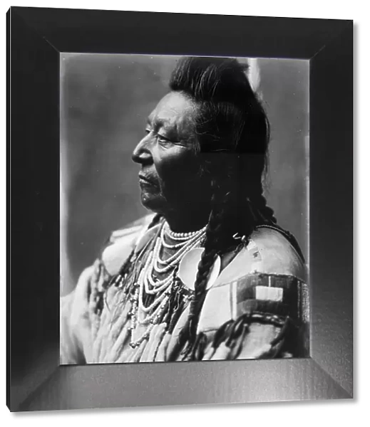 Plenty Coups, Crow Indian, head-and-shoulders portrait, facing left, pompadour, temple... c1908. Creator: Edward Sheriff Curtis