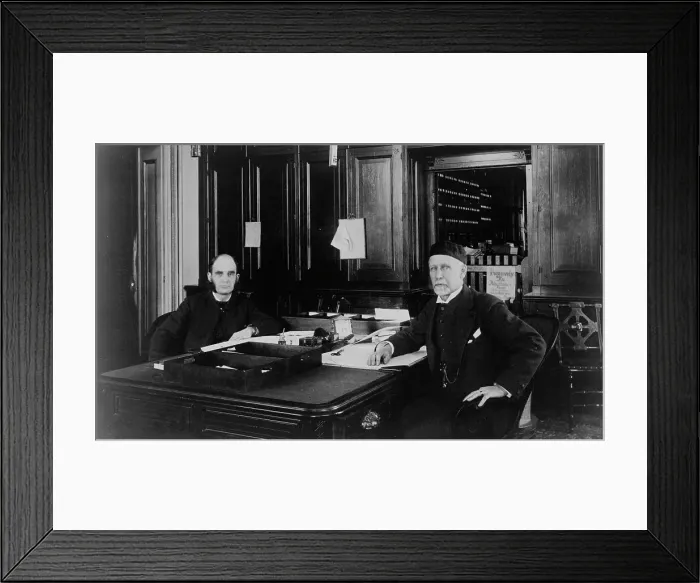 Framed Print : Two Treasury Department employees seated at desk in office, between 1884 and 1930. Creator: Frances Benjamin Johnston