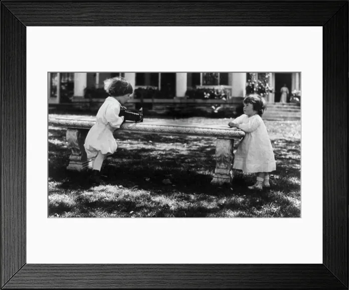 Framed Print : One child aiming camera, on bench, at another child, Washington, D.C. between c1890 and c1910. Creator: Frances Benjamin Johnston Framed Print : One child aiming camera, on bench, at another child, Washington, D.C. between c1890 and c1910. Creator: Frances Benjamin Johnston