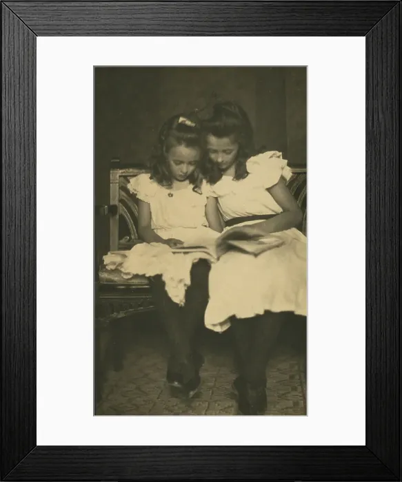 Framed Print : Two girls wearing white dresses and dark stockings reading a book, c1900. Creator: Virginia M Prall Framed Print : Two girls wearing white dresses and dark stockings reading a book, c1900. Creator: Virginia M Prall
