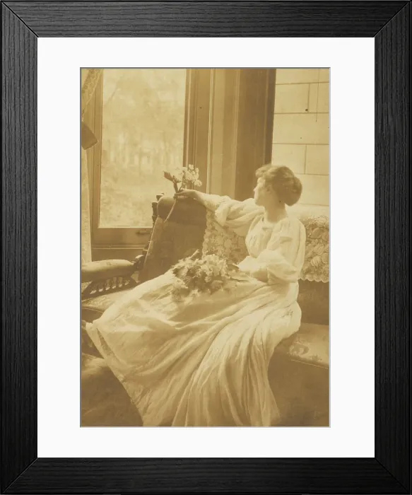 Framed Print : Young woman seated by a window with flowers in her lap, c1900. Creator: Mary A. Bartlett Framed Print : Young woman seated by a window with flowers in her lap, c1900. Creator: Mary A. Bartlett