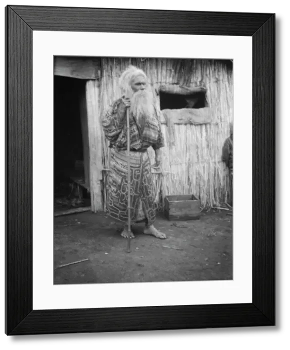 Framed Print : Ainu man holding a staff standing outside a hut, 1908. Creator: Arnold Genthe Framed Print : Ainu man holding a staff standing outside a hut, 1908. Creator: Arnold Genthe