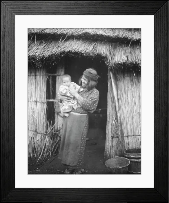 Framed Print : Ainu woman holding a child standing outside a hut, 1908. Creator: Arnold Genthe Framed Print : Ainu woman holding a child standing outside a hut, 1908. Creator: Arnold Genthe