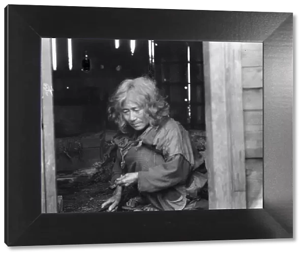 Ainu woman seated in the doorway of a wooden hut, 1908. Creator: Arnold Genthe