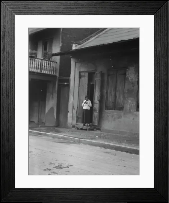 Framed Print : View from across street of a woman standing in a doorway in the French Quarter, New... c1920-c1926. Creator: Arnold Genthe Framed Print : View from across street of a woman standing in a doorway in the French Quarter, New... c1920-c1926. Creator: Arnold Genthe