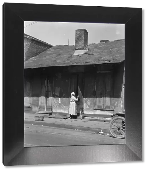 View from across street of a woman with a broom standing in a doorway, New Orleans, c1920-c1926. Creator: Arnold Genthe