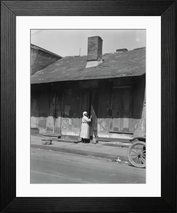 Framed Print : View from across street of a woman with a broom standing in a doorway, New Orleans, c1920-c1926. Creator: Arnold Genthe Framed Print : View from across street of a woman with a broom standing in a doorway, New Orleans, c1920-c1926. Creator: Arnold Genthe