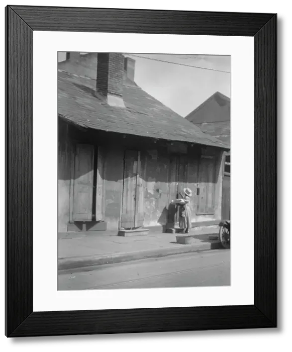 Framed Print : Woman holding a sack standing by the doorway of a building in the French Quarter... c1920-c1926. Creator: Arnold Genthe Framed Print : Woman holding a sack standing by the doorway of a building in the French Quarter... c1920-c1926. Creator: Arnold Genthe