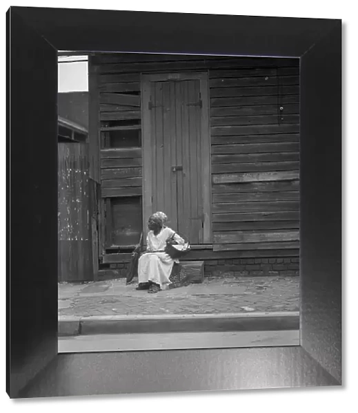 Woman sitting on steps holding a basket, New Orleans, between 1920 and 1926. Creator: Arnold Genthe