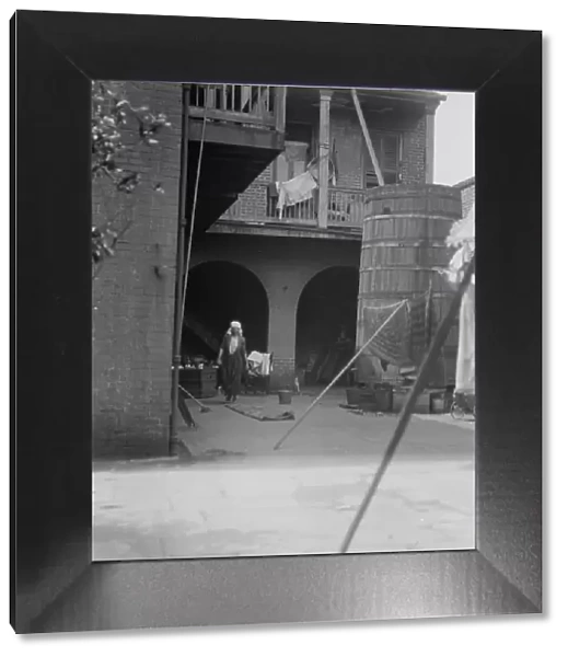 Courtyard with cistern and woman cleaning, New Orleans, between 1920 and 1926. Creator: Arnold Genthe