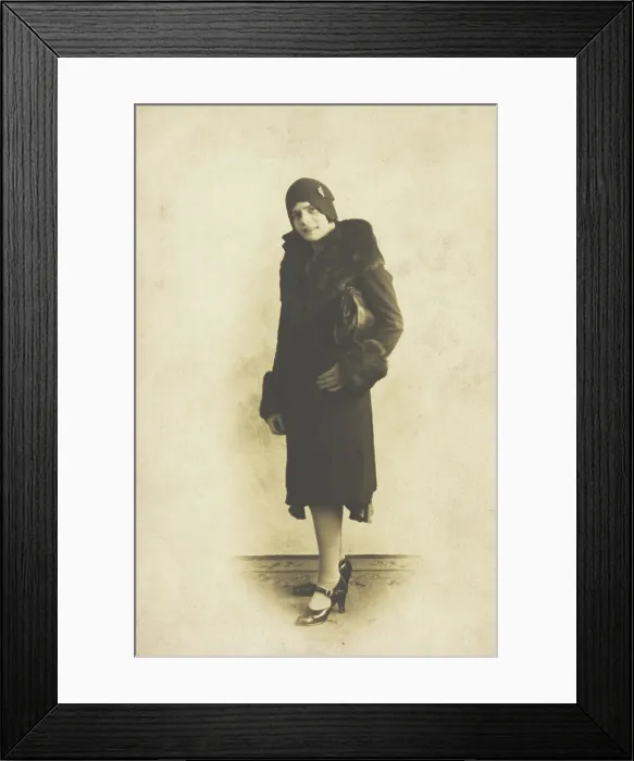 Framed Print : A person poses wearing a long coat with fur trim and a hat with a brooch, [between 1920 and 1929?]. Creator: Unknown