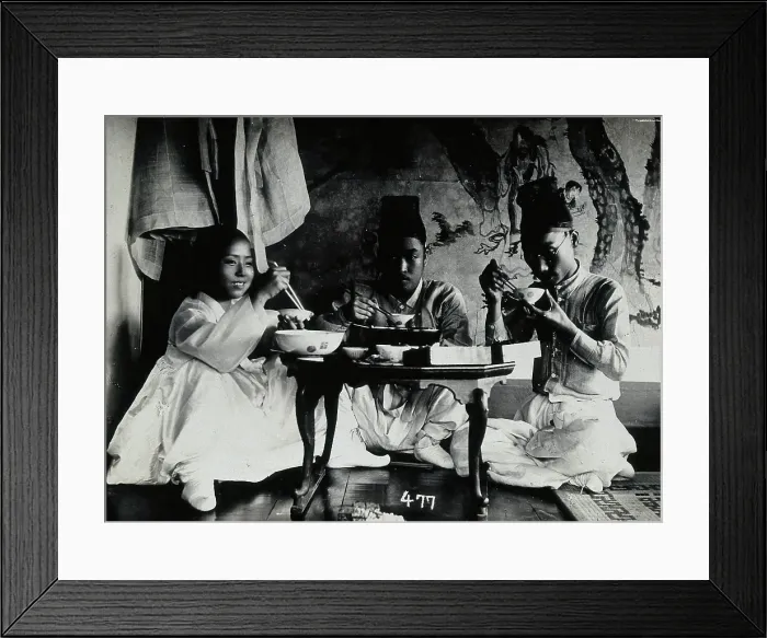 Framed Print : A group of people eating a meal, seated behind a small table, in front of a painted screen, c1900. Creator: Unknown Framed Print : A group of people eating a meal, seated behind a small table, in front of a painted screen, c1900. Creator: Unknown