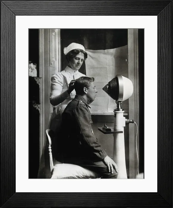 Framed Print : A young uniformed man sitting with a pillow on his chair, facing a machine... c1910s. Creator: Unknown Framed Print : A young uniformed man sitting with a pillow on his chair, facing a machine... c1910s. Creator: Unknown