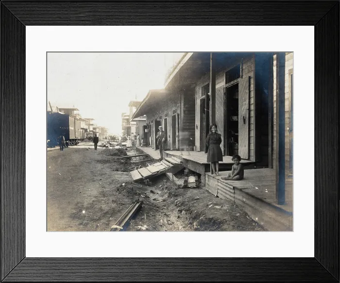 Framed Print : Colon, Panama: unpaved street lined with wooden houses; two children watch from a porch... 1906. Creator: Unknown
