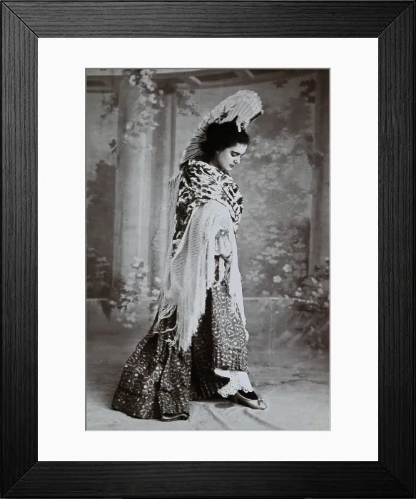 Framed Print : A standing woman, posed with an upraised fan and pointed toe, wearing a fringed shawl, in... c1900. Creator: Unknown Framed Print : A standing woman, posed with an upraised fan and pointed toe, wearing a fringed shawl, in... c1900. Creator: Unknown