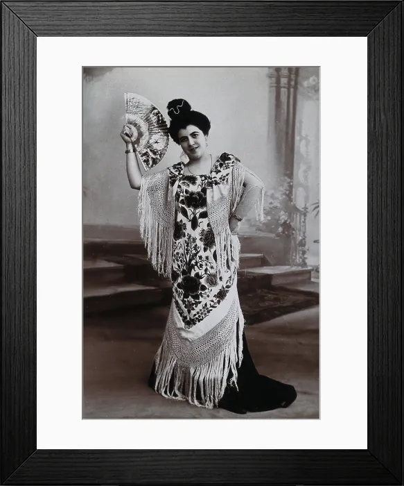 Framed Print : A standing woman, holding aloft a fan, wearing a fringed shawl, in front of a painted... c1900. Creator: Unknown Framed Print : A standing woman, holding aloft a fan, wearing a fringed shawl, in front of a painted... c1900. Creator: Unknown
