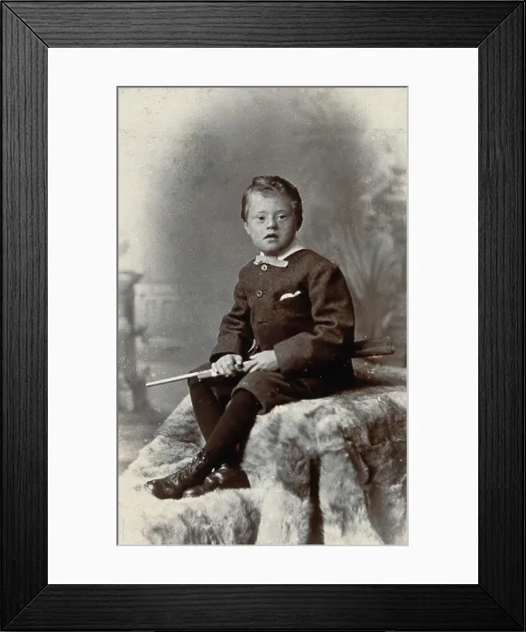 Framed Print : A boy with Down's syndrome, holding a rifle and sitting on a fur carpet, c1900 Framed Print : A boy with Down's syndrome, holding a rifle and sitting on a fur carpet, c1900