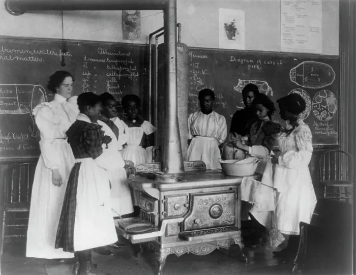 Framed Print : African American schoolgirls with teacher, learning to cook on a wood stove in classroom, (1899?). Creator: Frances Benjamin Johnston Framed Print : African American schoolgirls with teacher, learning to cook on a wood stove in classroom, (1899?). Creator: Frances Benjamin Johnston