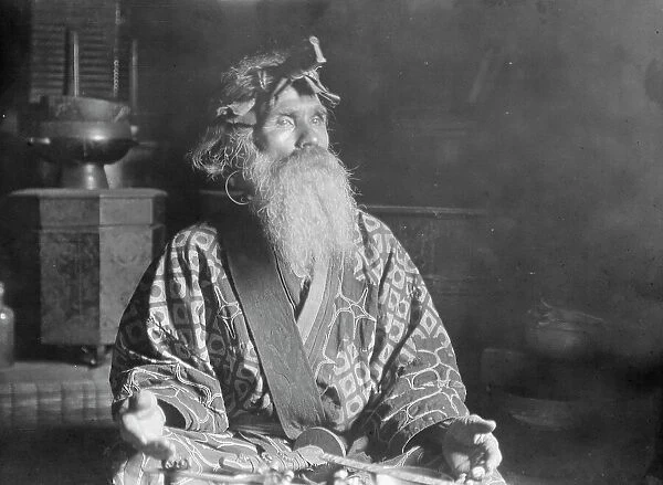 Ainu chief wearing a headdress seated with a sword in his lap, 1908. Creator: Arnold Genthe