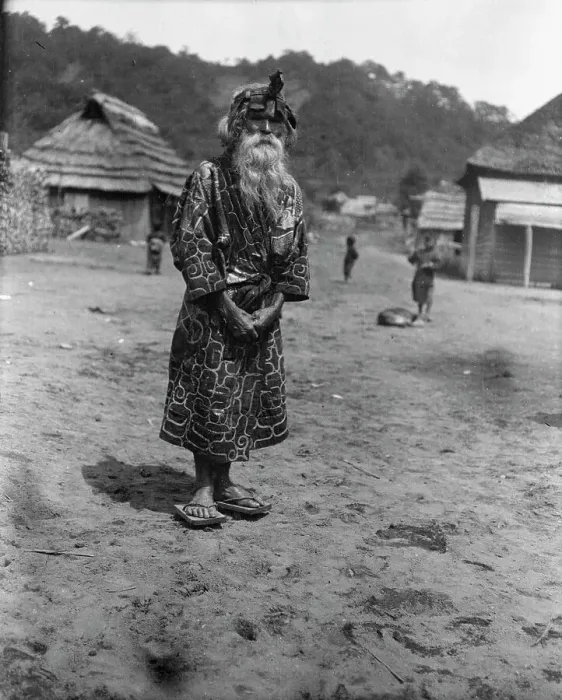 Framed Print : Ainu chief wearing a headdress standing in the village lane, 1908. Creator: Arnold Genthe