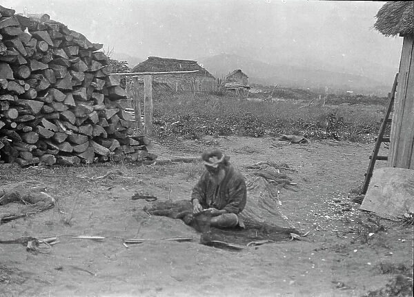 Ainu man seated outside working on nets, 1908. Creator: Arnold Genthe