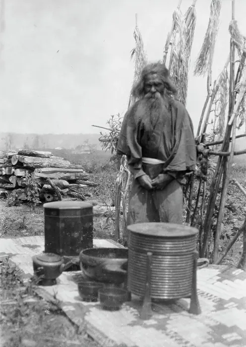 Framed Print : Ainu man standing outdoors on a mat covered with clay containers, 1908. Creator: Arnold Genthe