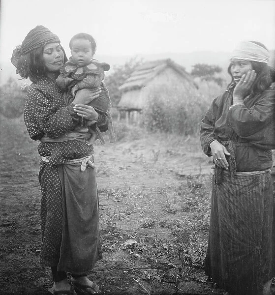 Two Ainu woman, one holding a child, standing outside, 1908. Creator: Arnold Genthe