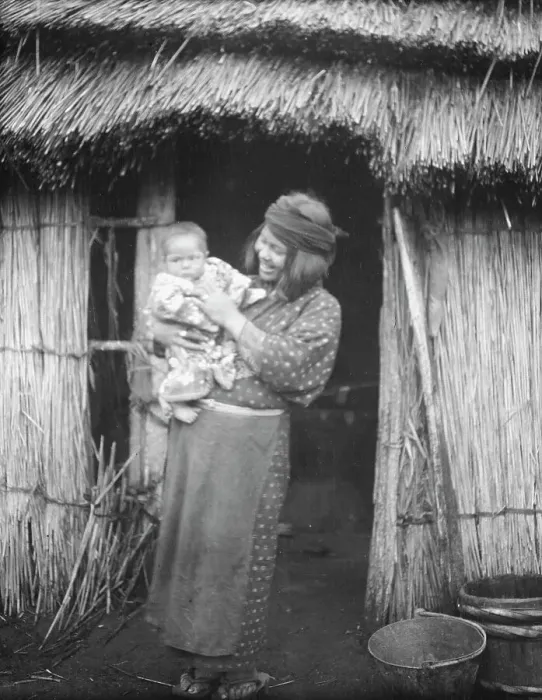 Framed Print : Ainu woman holding a child standing outside a hut, 1908. Creator: Arnold Genthe Framed Print : Ainu woman holding a child standing outside a hut, 1908. Creator: Arnold Genthe