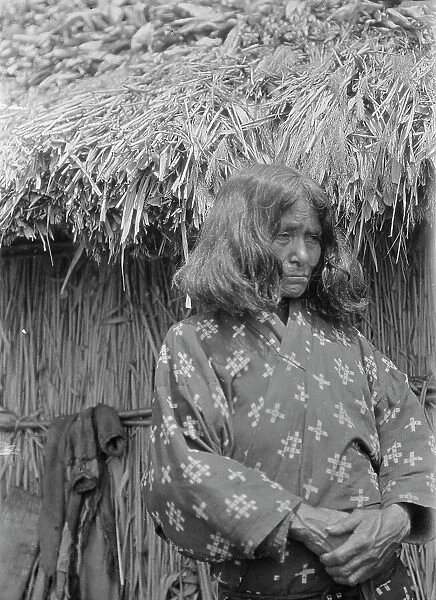 Ainu woman standing outside a hut, 1908. Creator: Arnold Genthe