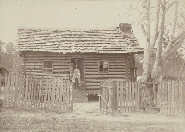 Albumen print of a woman and two children in front of a log house in Georgia, 1880s