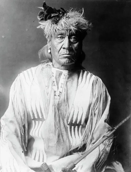 Framed Print : Atsina Indian, Red Whip, half-length portrait, seated, facing front, wearing feather... c1908. Creator: Edward Sheriff Curtis Framed Print : Atsina Indian, Red Whip, half-length portrait, seated, facing front, wearing feather... c1908. Creator: Edward Sheriff Curtis