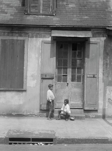Two children outside a door with shutters in the French Quarter, New Orleans, between 1920 and 1926. Creator: Arnold Genthe