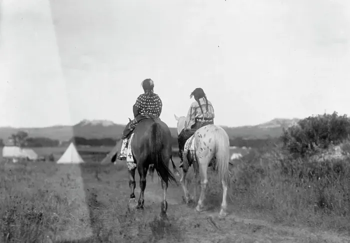Framed Print : Two daughters of a chief on horseback, riding away from camera toward tents in background, c1907. Creator: Edward Sheriff Curtis Framed Print : Two daughters of a chief on horseback, riding away from camera toward tents in background, c1907. Creator: Edward Sheriff Curtis