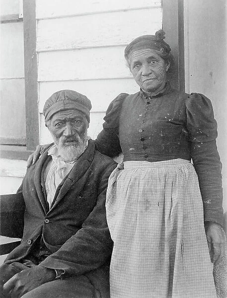 Elderly African American couple posed outside of building, near Hampton Institute... 1899 or 1900. Creator: Frances Benjamin Johnston