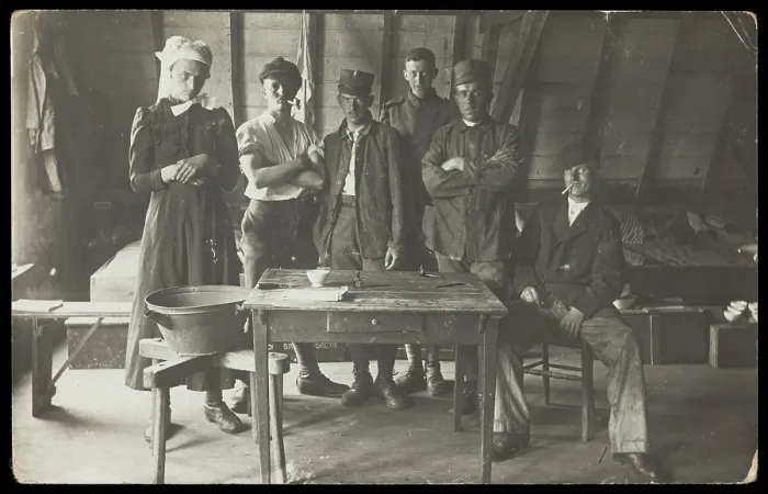 Framed Print : French prisoners of war, one in drag, gather round a small wooden table, [between 1910 and 1919?]. Creator: Unknown
