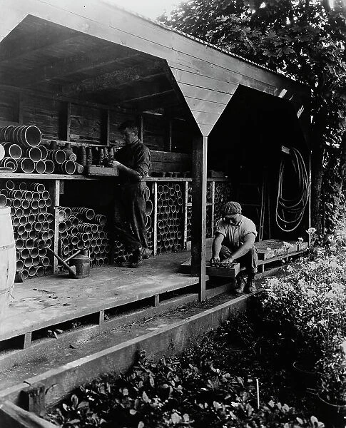 Gardeners potting plants in a shed, posed to...Rudyard Kipling's poem The Glory of the Garden, 1917. Creator: Frances Benjamin Johnston