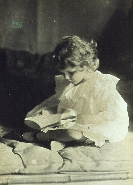 Girl sitting with legs folded, reading a book, c1900. Creator: Eva Watson-Schutze