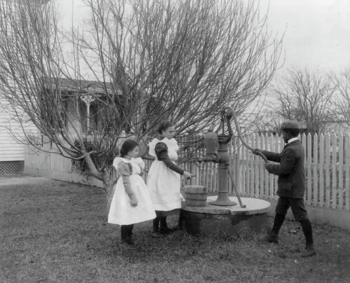 Framed Print : Two girls and a boy pumping water at well of Hampton Institute graduate, 1899 or 1900. Creator: Frances Benjamin Johnston Framed Print : Two girls and a boy pumping water at well of Hampton Institute graduate, 1899 or 1900. Creator: Frances Benjamin Johnston